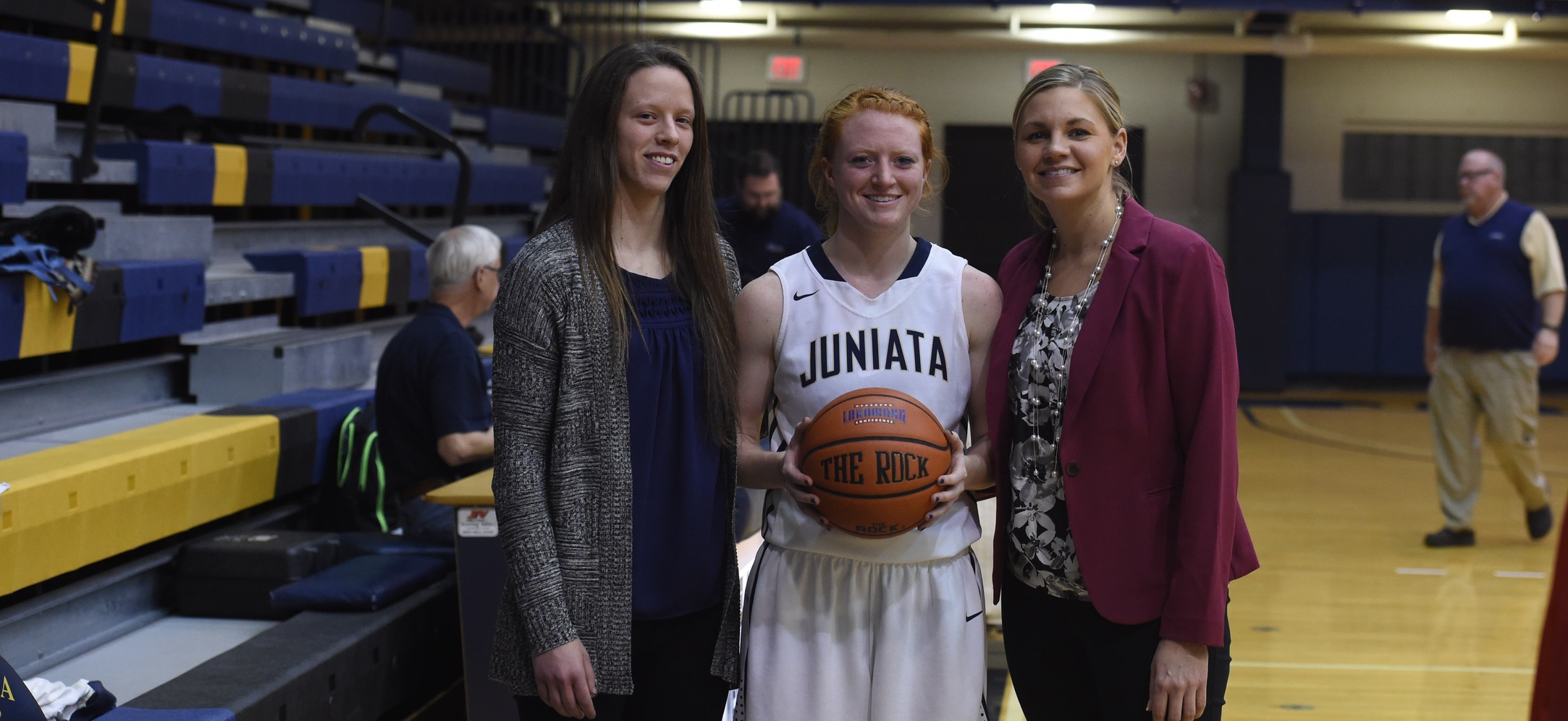 Dani Atkinson holding the ball she scored her 1,00th point with, standing in-between head coach Danny Young-Uhrich and assistant coach Kate McDonald.